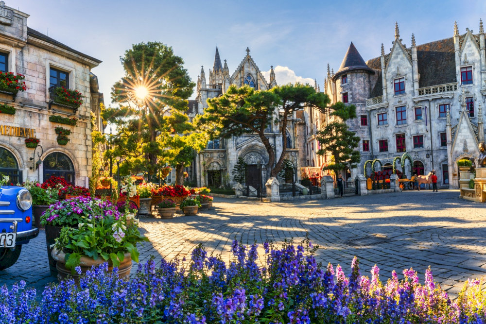 The charming French Village, bathed in the morning sunlight, is surrounded by a vibrant garden of colorful flowers 